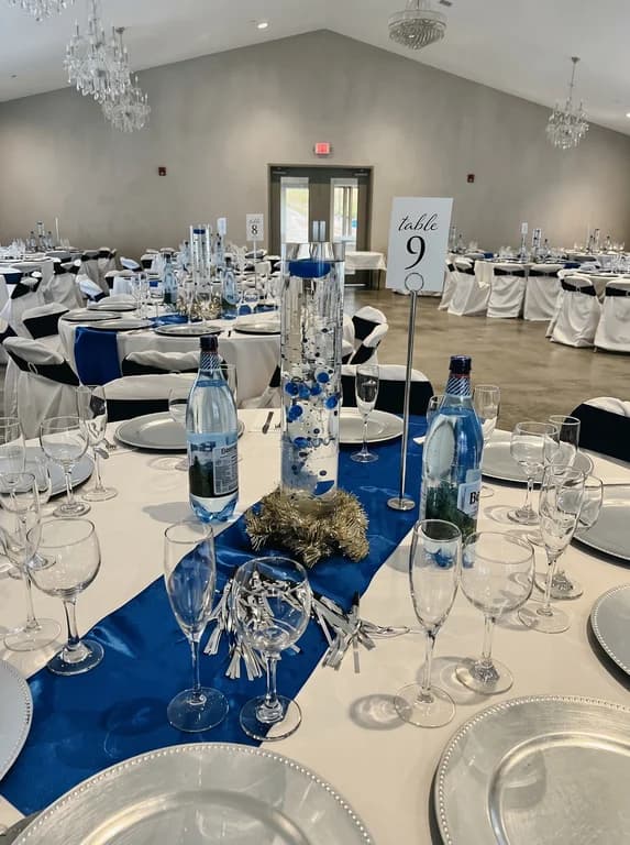 Close-up place setting with a navy blue runner, silver charger plates and a table number card