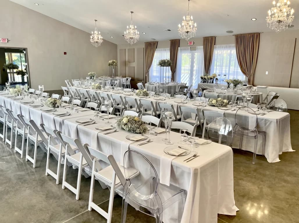 Long reception tables with white linens, clear ghost chairs and baby's breath centerpieces in the main hall