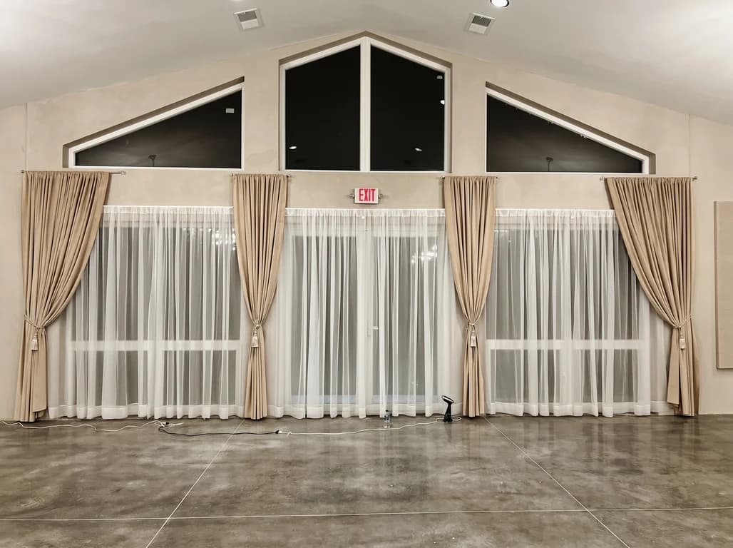 Floor-to-ceiling sheer draping and gold curtains along the window wall of the empty hall