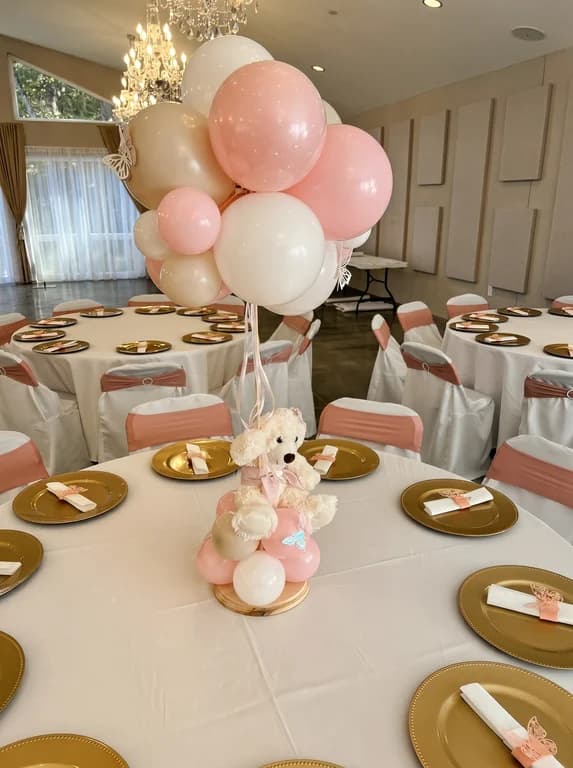 Baby shower table with gold chargers, a teddy bear centerpiece and pink and white balloons