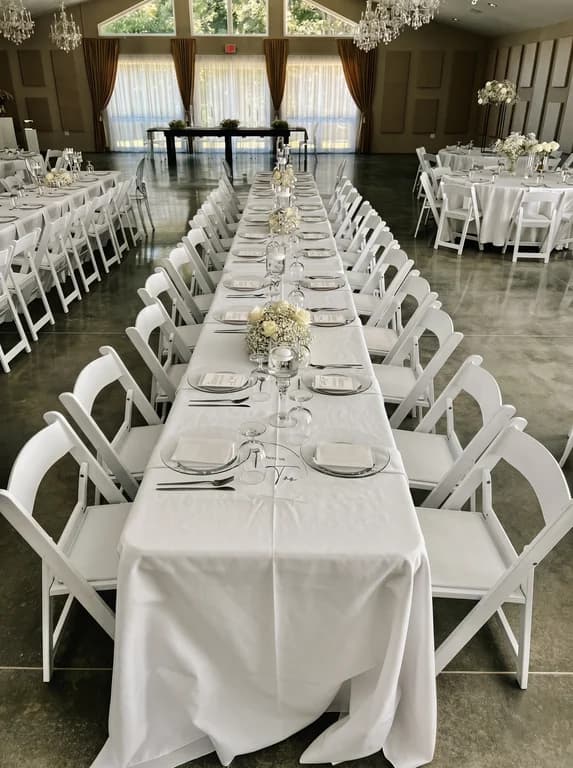 Long white banquet table lined with folding chairs and baby's breath centerpieces