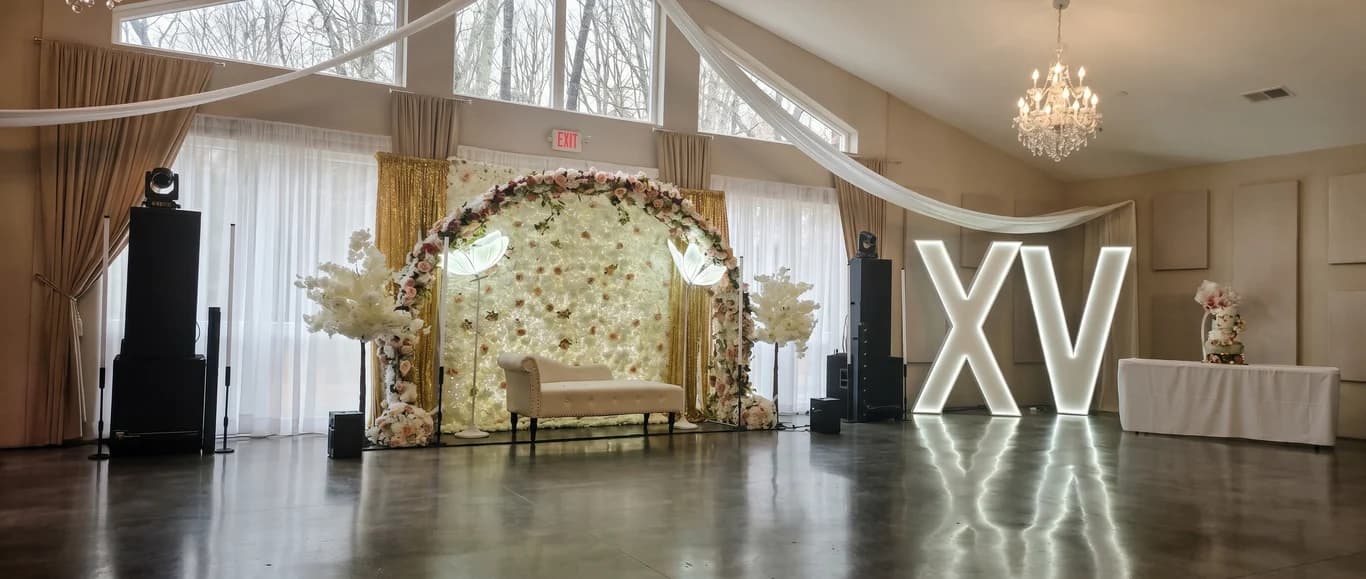 Quinceañera setup with a floral arch, marquee XV letters and draped ceiling in the main hall